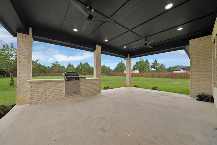 The property features an expansive outdoor patio with a built-in grill, overhead lighting, and two ceiling fans