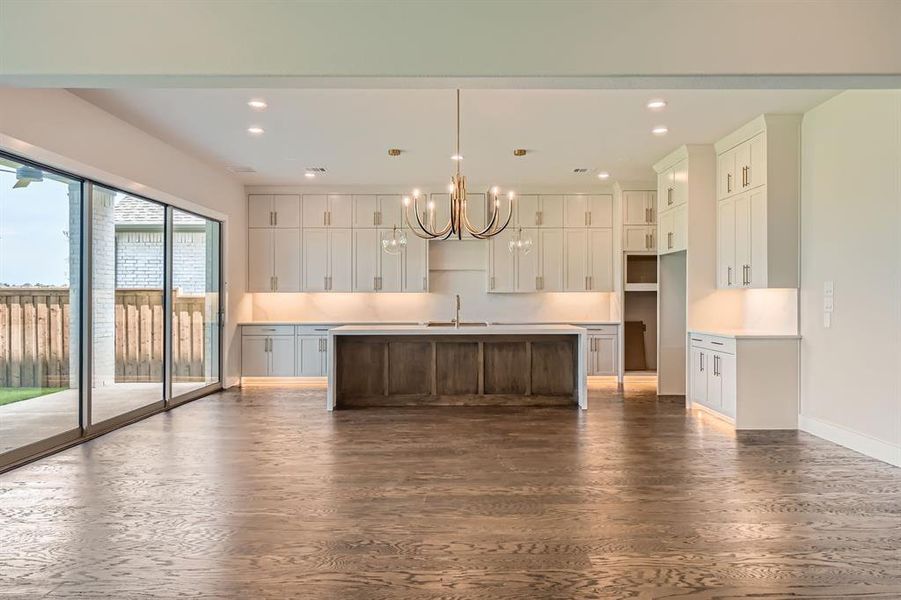 Kitchen with dark wood-style flooring, a chandelier, a center island with sink, white cabinets, and recessed lighting Kitchen with dark wood-style flooring, a chandelier, a center island with sink, white cabinets, and recessed lighting