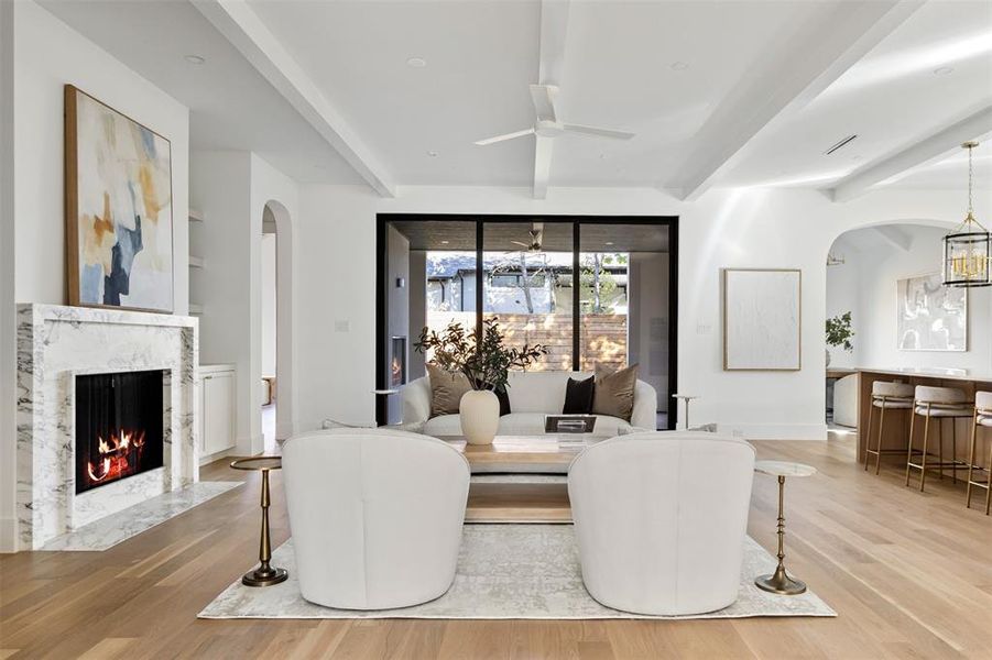 Dining space with arched walkways, light wood finished floors, a high end fireplace, ceiling fan, and beamed ceiling Dining space with arched walkways, light wood finished floors, a high end fireplace, ceiling fan, and beamed ceiling