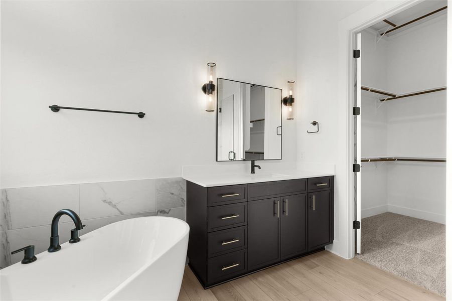 Full bathroom featuring vanity, a freestanding tub, light wood-type flooring, a walk in closet, and tile walls