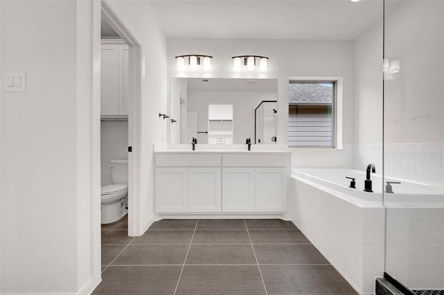 Bathroom featuring a garden tub, dark tile patterned floors, double vanity, and a stall shower