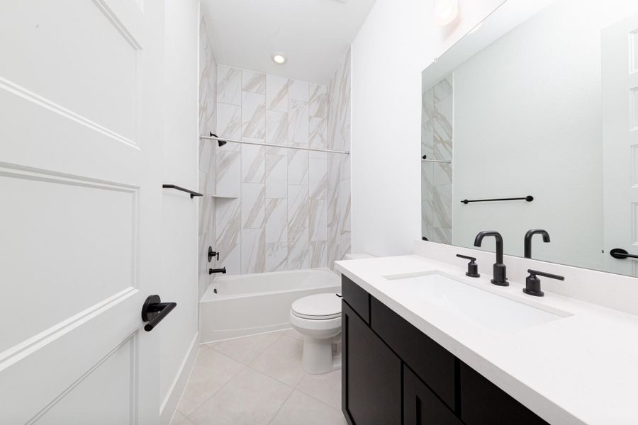 This ensuite secondary bathroom features a modern vanity, tub/shower combination with gorgeous tile surround, and modern black matte finishes.