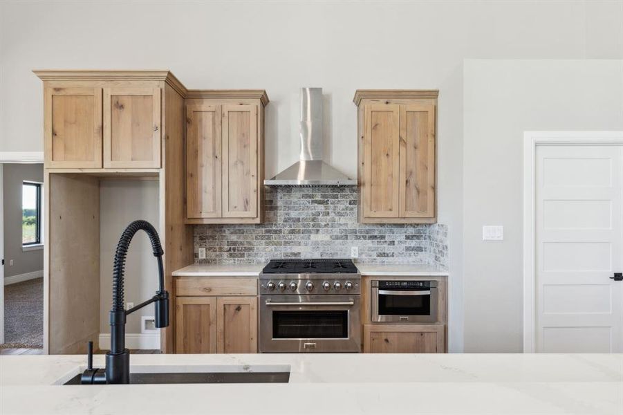 Kitchen featuring stainless steel appliances, light countertops, backsplash, a sink, and exhaust hood Kitchen featuring stainless steel appliances, light countertops, backsplash, a sink, and exhaust hood