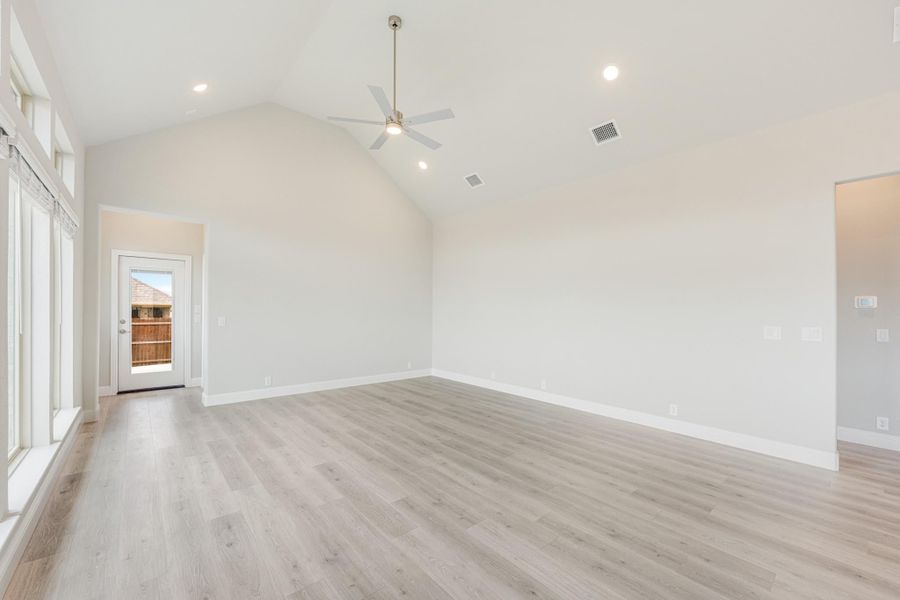 Empty living room with vaulted ceiling, ceiling fan, light wood floors, and back door access