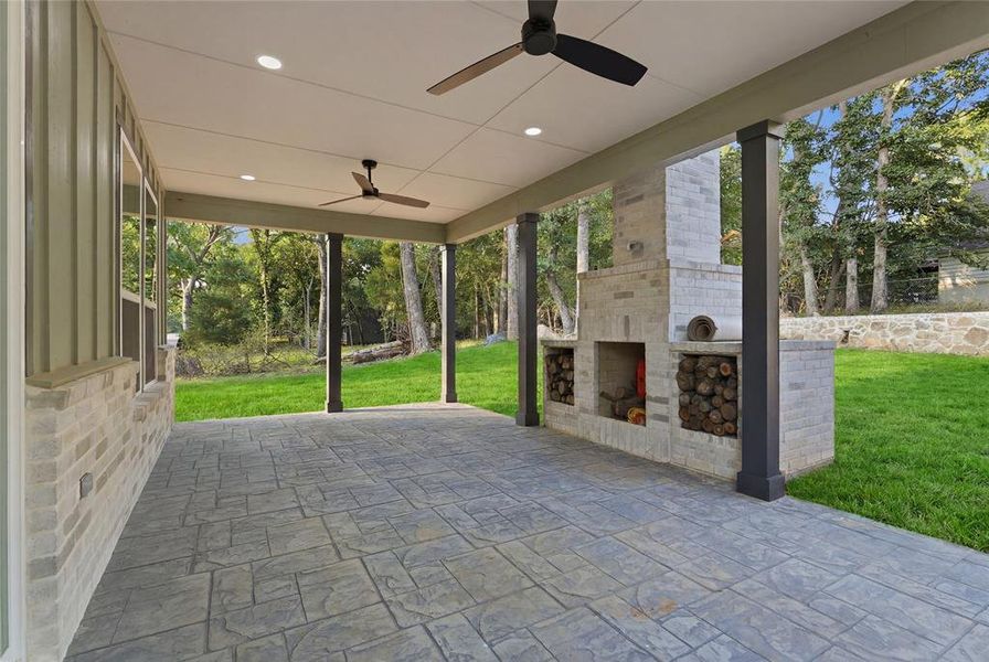 Spacious covered patio featuring a stamped concrete surface, integrated outdoor fireplace with stone surround, recessed lighting, and dual ceiling fans Spacious covered patio featuring a stamped concrete surface, integrated outdoor fireplace with stone surround, recessed lighting, and dual ceiling fans