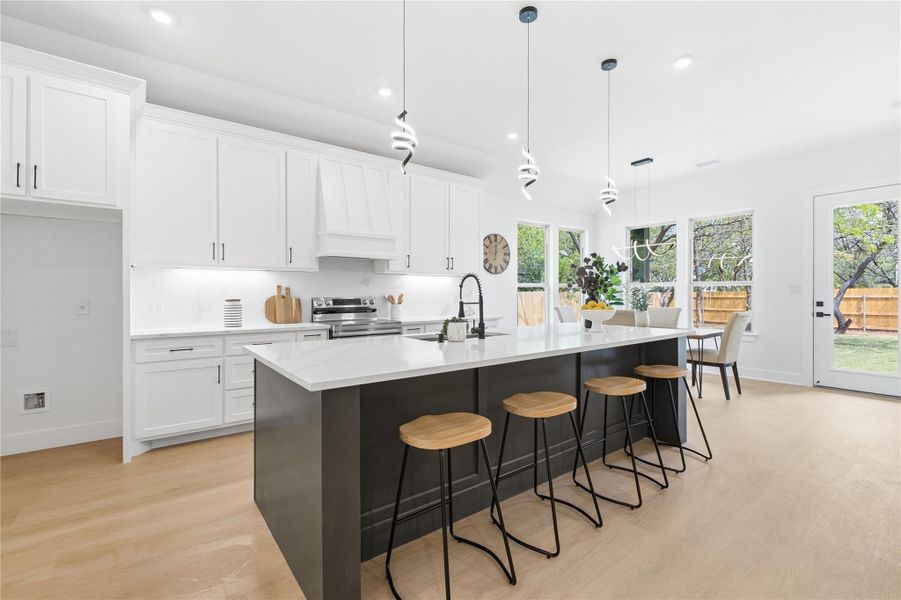 Kitchen featuring a kitchen breakfast bar, decorative light fixtures, two tone cabinetry, a center island with sink, and light wood-style floors