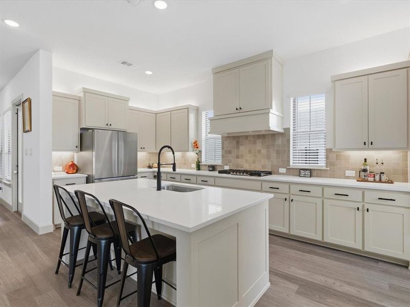 Kitchen featuring an expansive center island with seating, light-toned cabinetry, stainless steel appliances, and wood-finish flooring