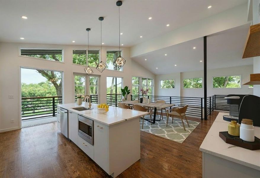 Kitchen with pendant lighting, light stone countertops, dark wood-style floors, white cabinetry, and high vaulted ceiling