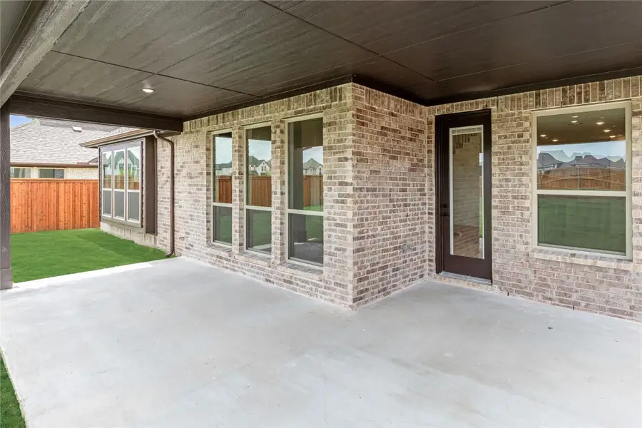 Covered back patio with concrete slab, brick exterior, back door, and fenced yard with green lawn