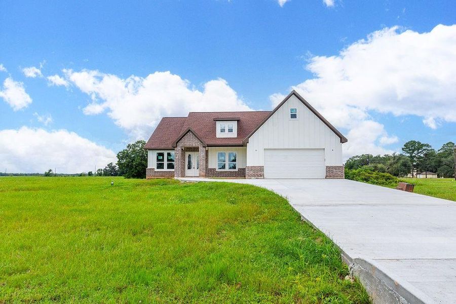 Charming modern farmhouse with a spacious lawn, featuring a welcoming brick and siding exterior, and a large driveway leading to an attached garage. Charming modern farmhouse with a spacious lawn, featuring a welcoming brick and siding exterior, and a large driveway leading to an attached garage.