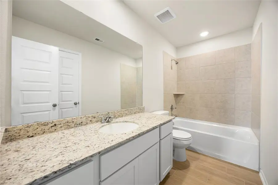 This secondary bathroom is clean, bright, and functionally designed. It features a single vanity with white shaker-style cabinetry, a granite countertop, a large mirror, and a tub/shower combo with tile surround. This secondary bathroom is clean, bright, and functionally designed. It features a single vanity with white shaker-style cabinetry, a granite countertop, a large mirror, and a tub/shower combo with tile surround.