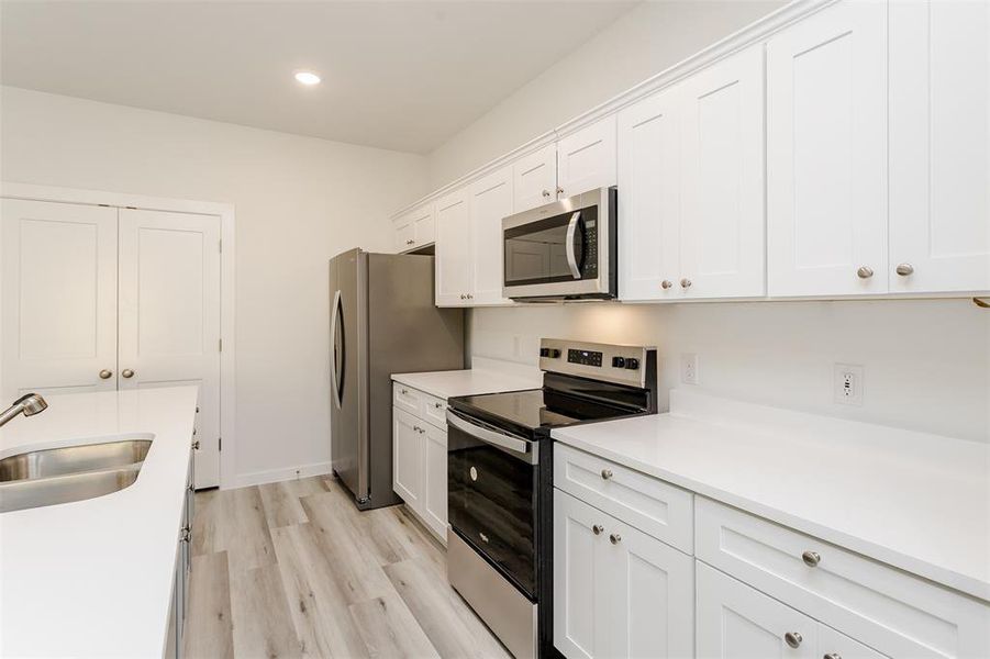 Kitchen featuring sink, white cabinets, light wood-type flooring, and appliances with stainless steel finishes