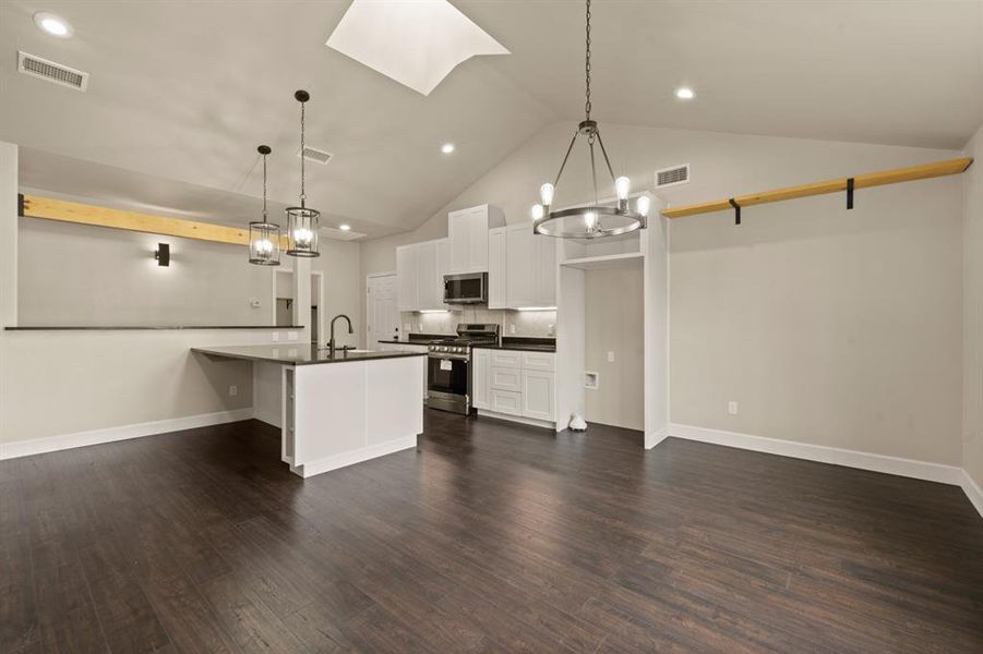 Kitchen featuring stainless steel appliances, dark countertops, a chandelier, a sink, and high vaulted ceiling