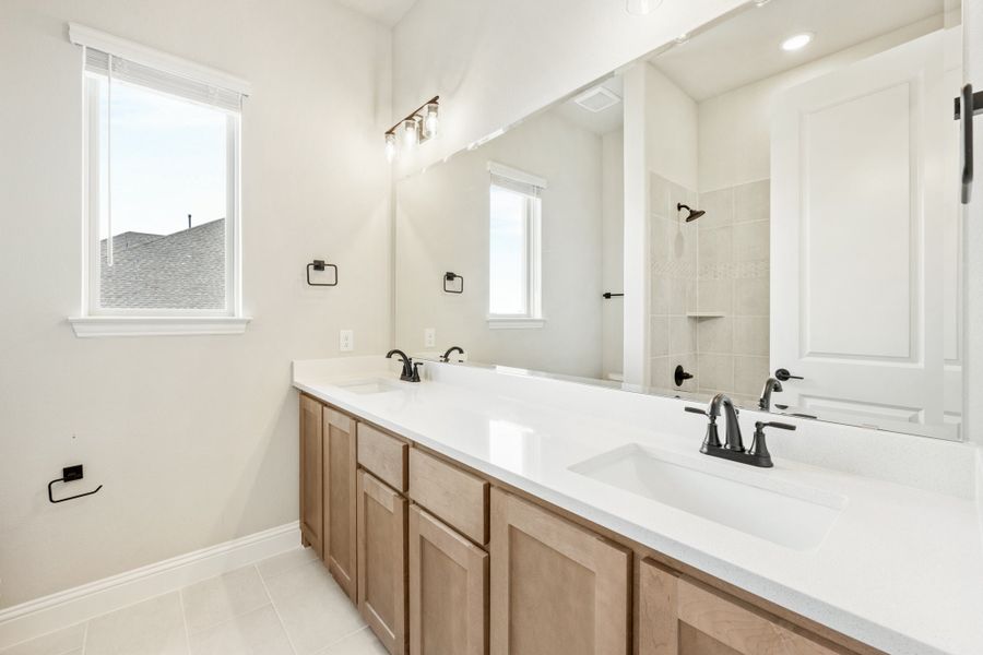 Bathroom with double vanity, wood cabinets, white countertops, large mirror, and tiled shower in background. Bathroom with double vanity, wood cabinets, white countertops, large mirror, and tiled shower in background.
