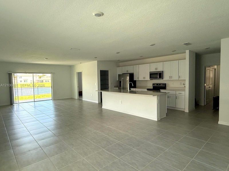 Open-concept interior featuring large-format neutral tile flooring, white shaker-style cabinetry, solid-surface countertops, recessed lighting, and sliding glass doors
