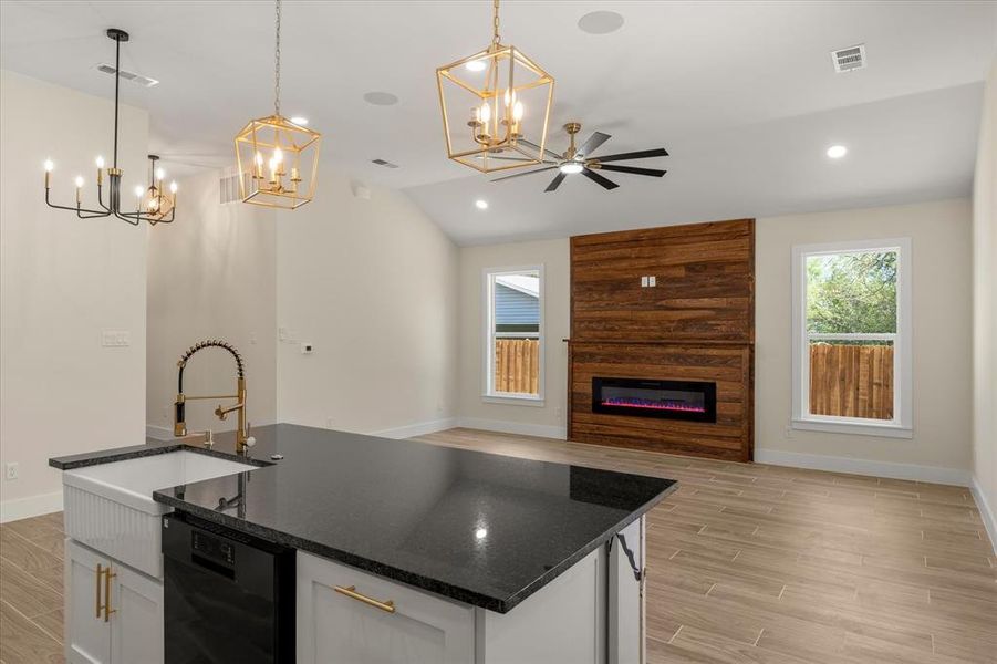 Open Livingwith a center island with sink, dark stone counters, wood tiled floors, white cabinets, and lofted ceiling