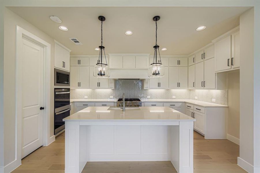 Kitchen with recessed lighting, a center island with sink, decorative backsplash, white cabinets, and hanging light fixtures