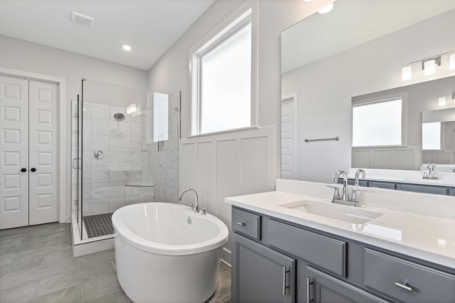 Freestanding soaking tub, walk-in shower with clear glass enclosure and tile surround, dual vanity with undermount sinks and light-toned countertops, and paneled wall detailing