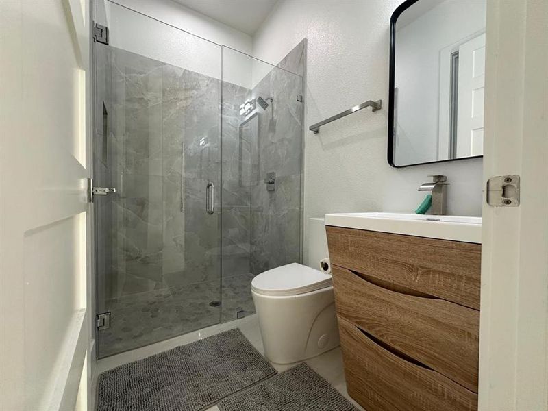 Bathroom with toilet, a shower with door, and vanity