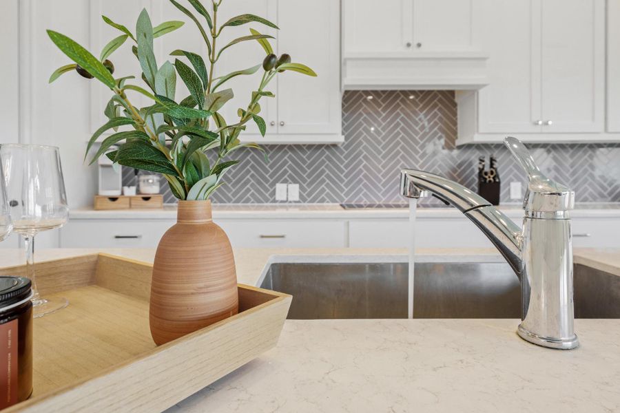This kitchen features a modern design with a sleek faucet over a stainless steel sink, set against a stylish herringbone tile backsplash.