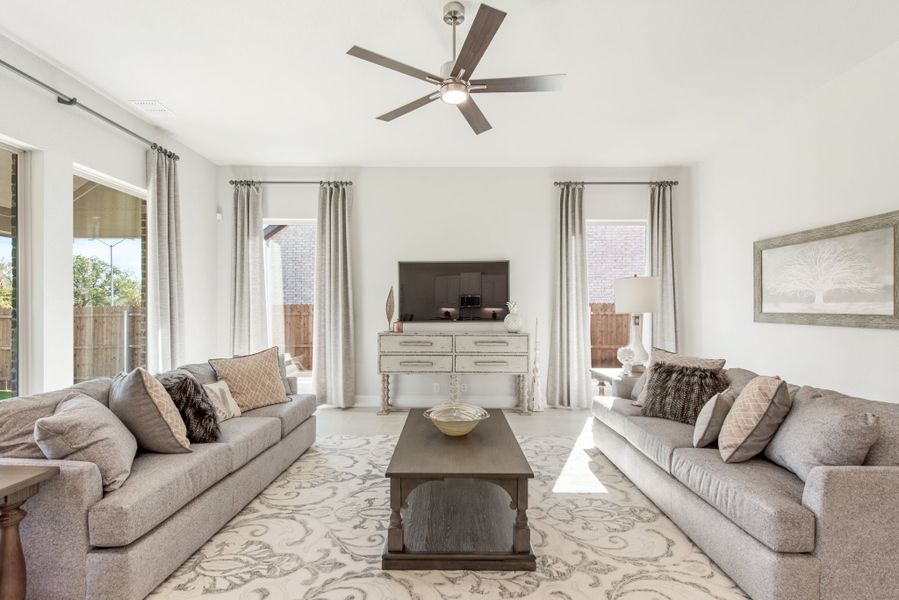 Bright living room with two gray sofas, ceiling fan, patterned area rug, and wall-mounted TV Bright living room with two gray sofas, ceiling fan, patterned area rug, and wall-mounted TV
