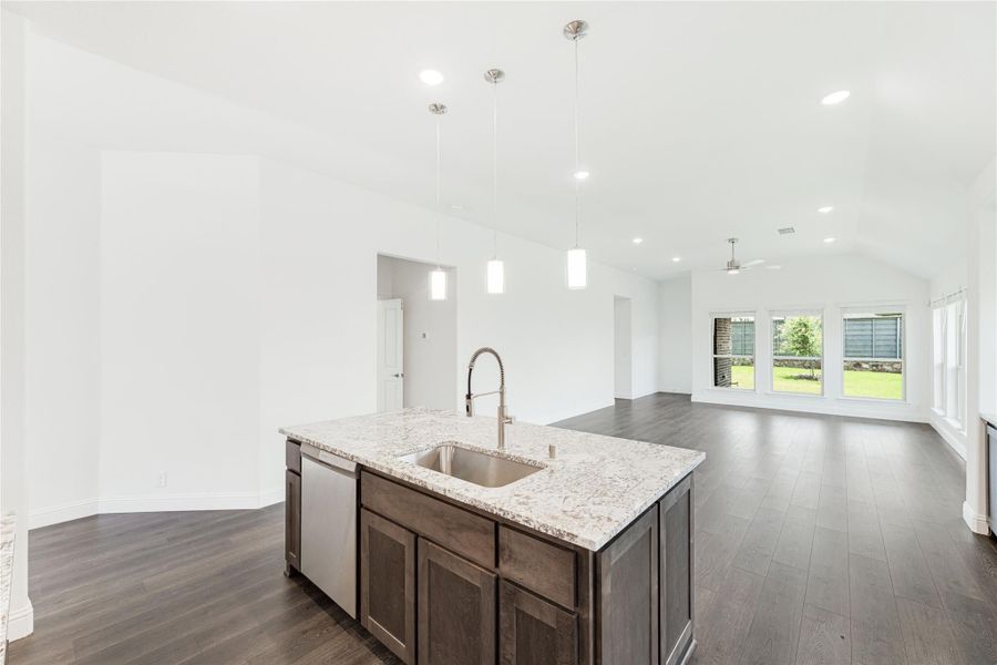 Kitchen island with granite countertop and sink, dark wood cabinets, pendant lights, and open living area with hardwood floors Kitchen island with granite countertop and sink, dark wood cabinets, pendant lights, and open living area with hardwood floors