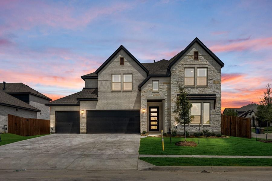 Two-story home with stone and brick exterior, three-car garage, and green front lawn at dusk