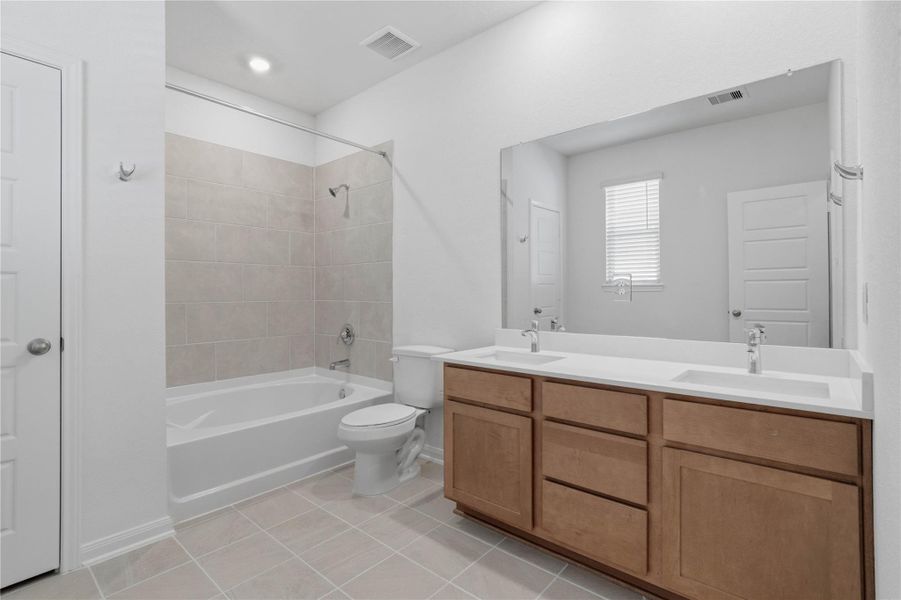 Luxurious primary suite bath boasts a large double sink vanity topped with elegant countertops and tub/shower combination with tile surround.