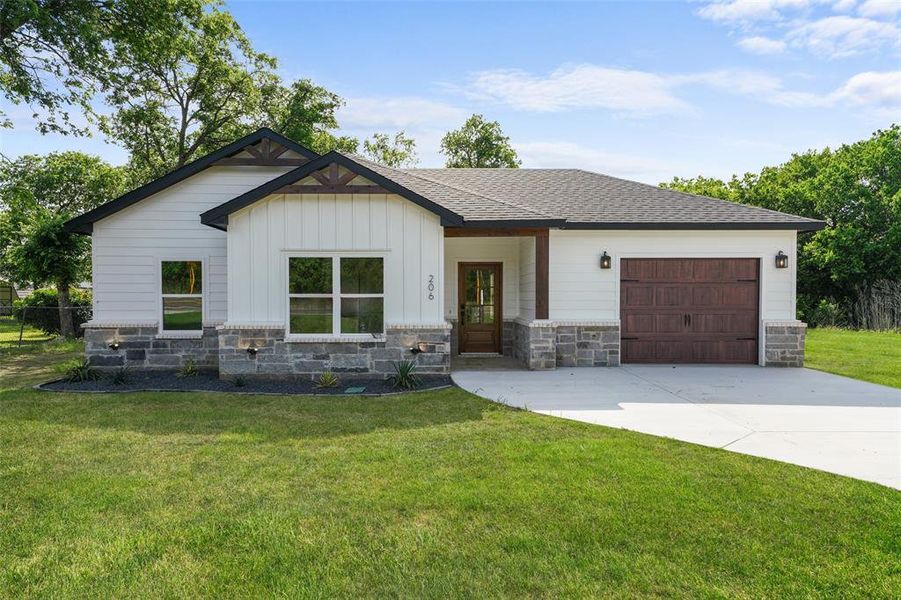 Modern farmhouse exterior featuring white siding, dark gray stone accents, a dark wood-finish garage door, and a covered entry with a glass-paneled door