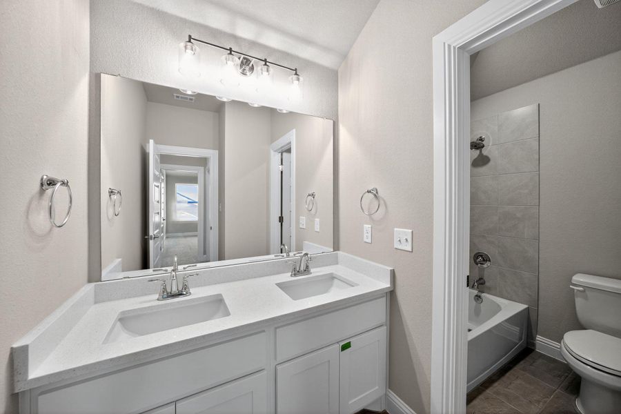 Bathroom featuring bathing tub / shower combination, double vanity, a textured wall, and dark tile patterned floors Bathroom featuring bathing tub / shower combination, double vanity, a textured wall, and dark tile patterned floors