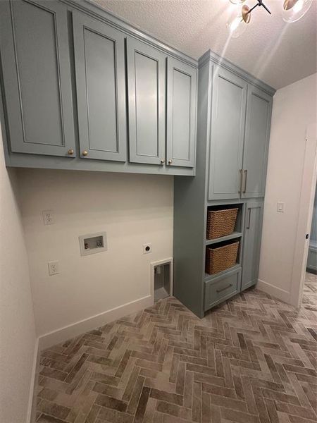 Laundry area featuring herringbone-patterned floor tiles, extensive cabinetry with crown molding, and modern light fixture