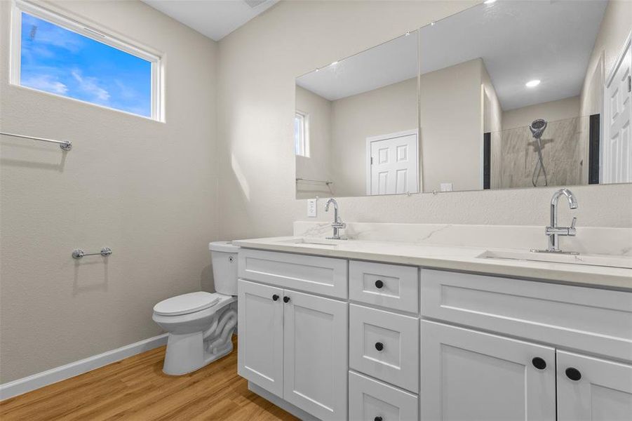 Full bathroom with double vanity, light wood finished floors, and a tile shower