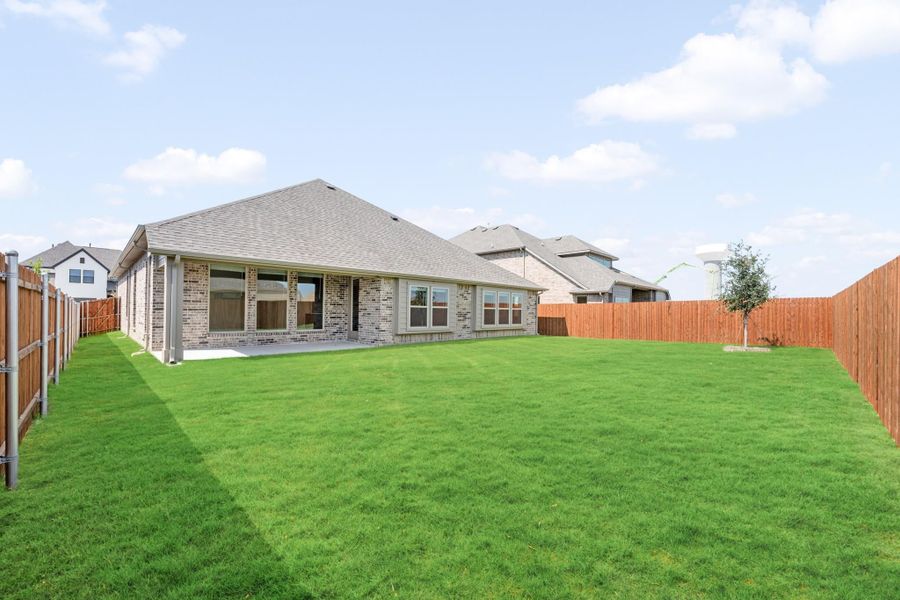 Backyard of brick home with large green lawn, wood privacy fence, and covered patio