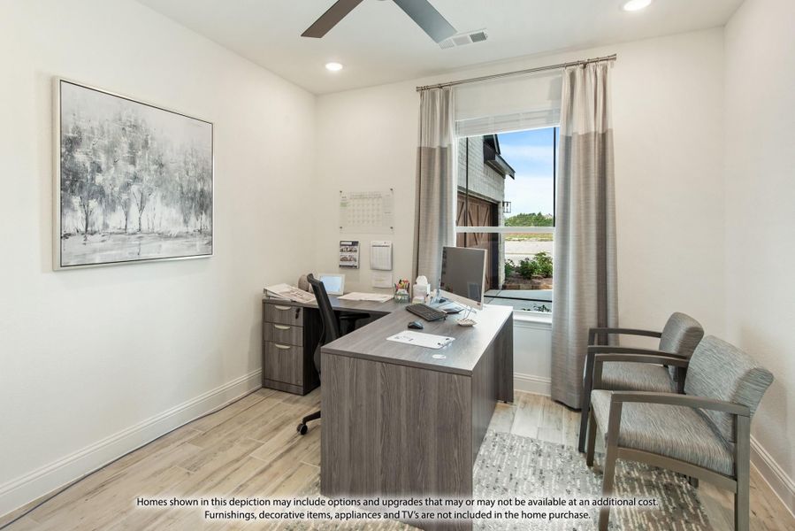 Home office with L-shaped wood desk, ceiling fan, light hardwood floors, and a large window with gray curtains Home office with L-shaped wood desk, ceiling fan, light hardwood floors, and a large window with gray curtains