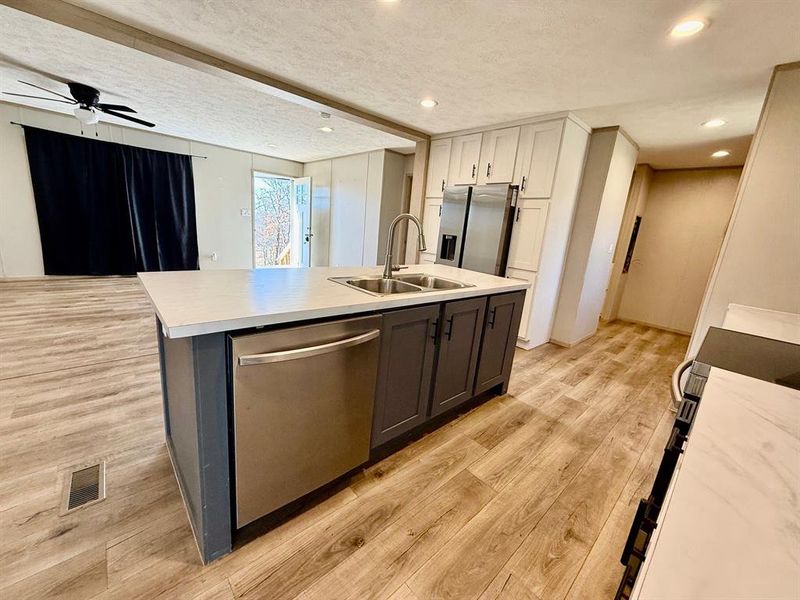 Dual tone kitchen with two tone cabinetry, a center island with sink, stainless steel appliances, light wood-style floors, and light countertops Dual tone kitchen with two tone cabinetry, a center island with sink, stainless steel appliances, light wood-style floors, and light countertops