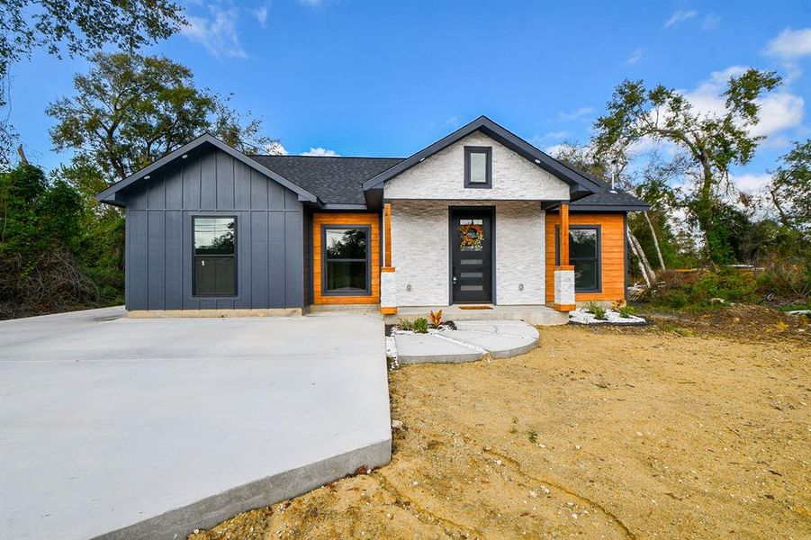 Welcome to this charming modern single-story home! It showcases beautiful siding, a lovely white stone facade, and a warm wooden accent that frames the front door, creating a welcoming entrance.