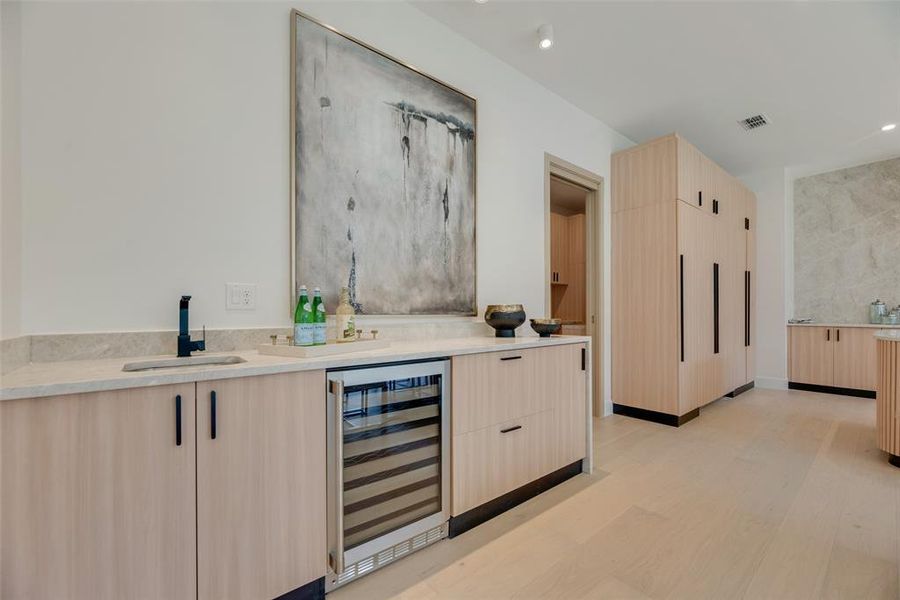 Bar with light brown cabinets, wine cooler, sink, and light wood-type flooring