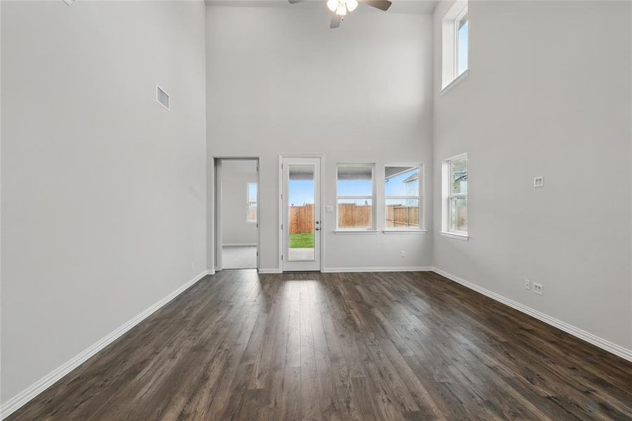 Empty room featuring dark wood-type flooring, a towering ceiling, and ceiling fan
