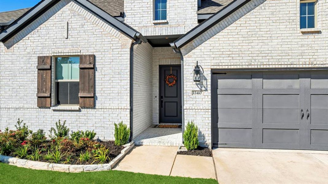 Doorway to property with brick siding, concrete driveway, and a shingled roof