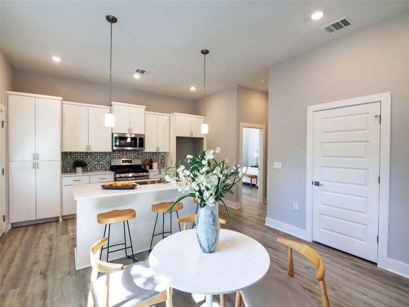 Kitchen featuring white cabinets, pendant lighting, appliances with stainless steel finishes, a breakfast bar, and light wood-style flooring
