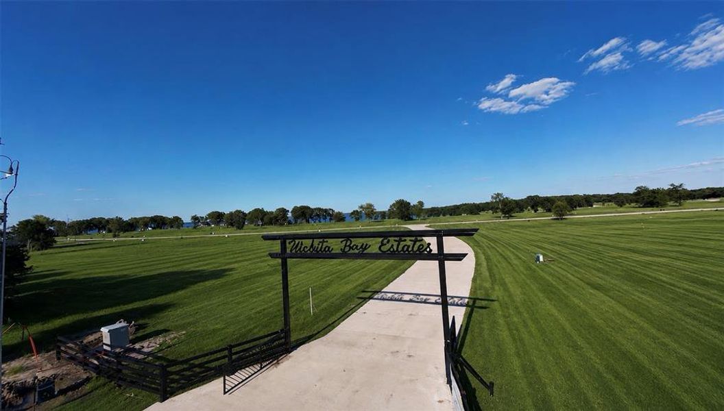 Entry gate featuring a paved drive, black metal signage, and perimeter fencing Entry gate featuring a paved drive, black metal signage, and perimeter fencing