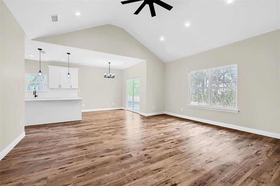 Unfurnished living room with sink, high vaulted ceiling, wood-type flooring, and ceiling fan with notable chandelier