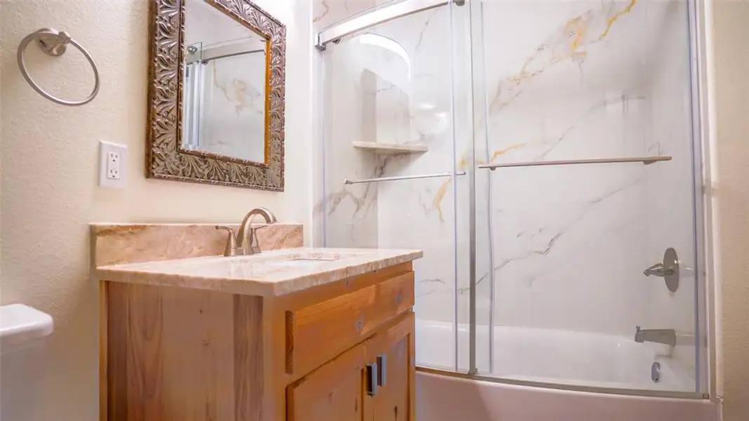 Bathroom featuring a textured wall, quartzite vanity, and combined bath / shower with glass door Bathroom featuring a textured wall, quartzite vanity, and combined bath / shower with glass door