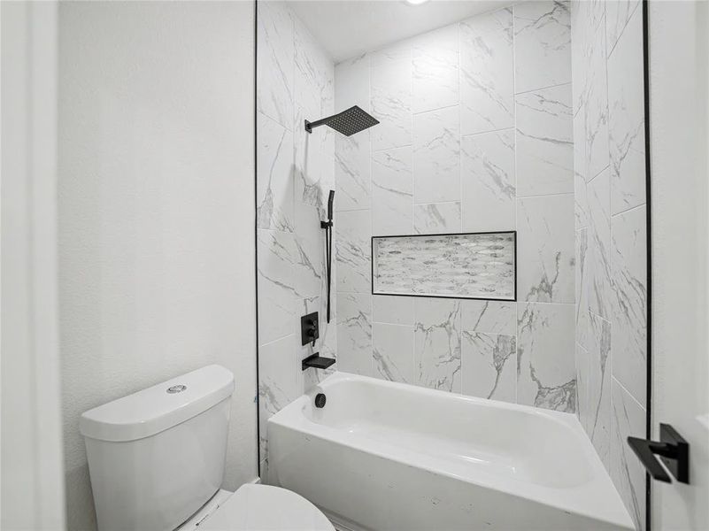 Modern bathroom featuring a bathtub with a rainfall showerhead, white marble-look tile surround, recessed tile niche, and matte black fixtures Modern bathroom featuring a bathtub with a rainfall showerhead, white marble-look tile surround, recessed tile niche, and matte black fixtures