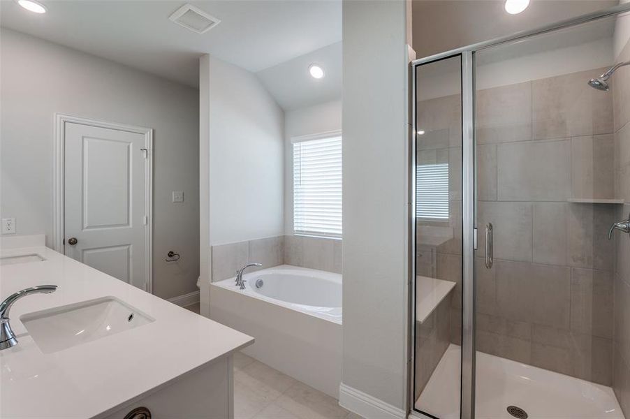 Bathroom featuring a dual vanity with undermount sinks, a soaking tub with window, and a glass-enclosed shower with tile surround and built-in bench