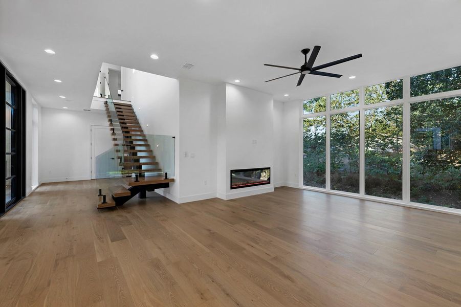 Unfurnished living room with a wall of windows, a glass covered fireplace, light wood finished floors, recessed lighting, and stairs