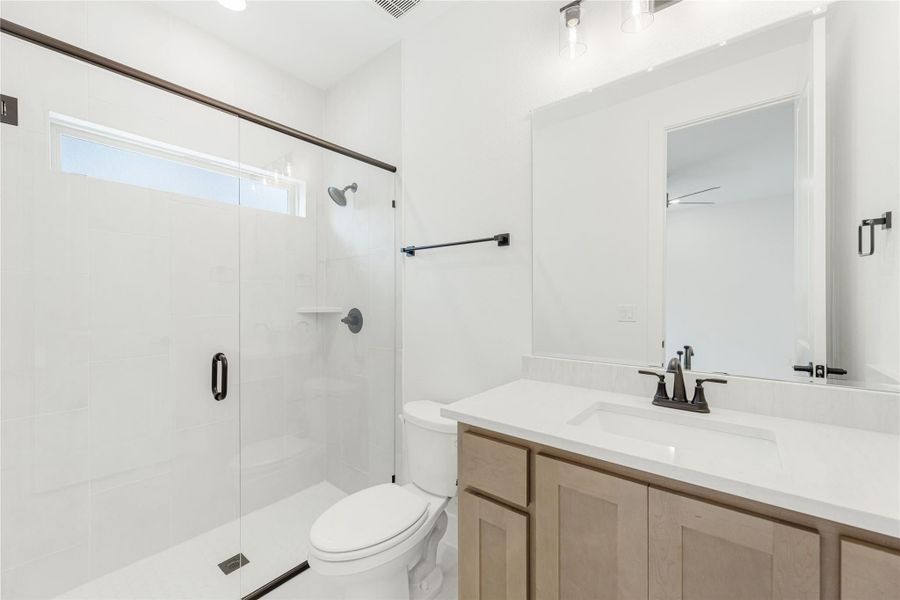 Bathroom with glass walk-in shower, white tile walls, wood vanity, and black hardware accents