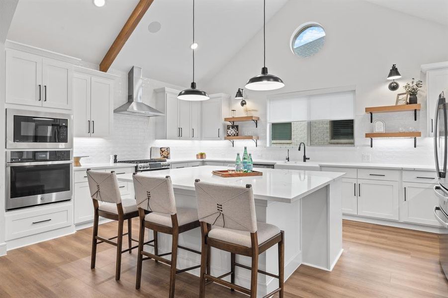 Kitchen with open shelves, white cabinets, stainless steel appliances, a kitchen breakfast bar, and decorative light fixtures