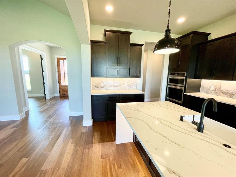 Kitchen with decorative backsplash, light hardwood / wood-style flooring, pendant lighting, light stone countertops, and double oven