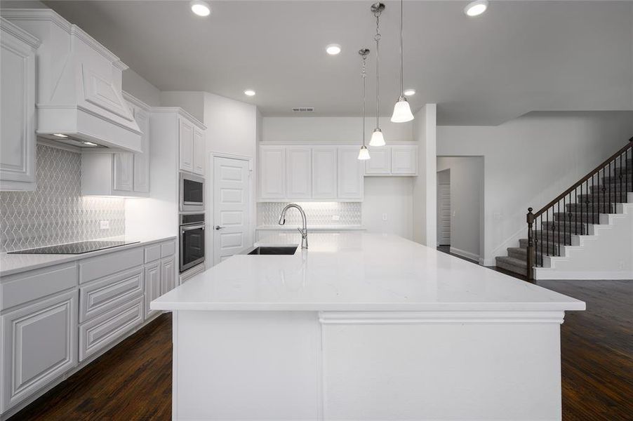 Kitchen with dark hardwood / wood-style floors, white cabinets, a kitchen island with sink, and sink